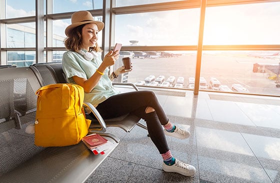 Young lady sitting in airport using mobile banking