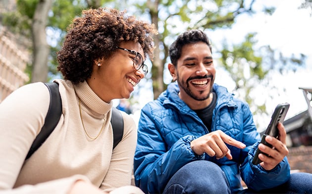 Couple sitting down looking at a phone. 