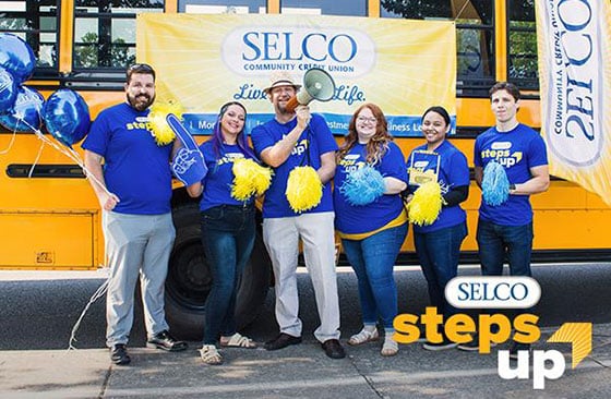 SELCO staff standing in front of a school bus holding signs.