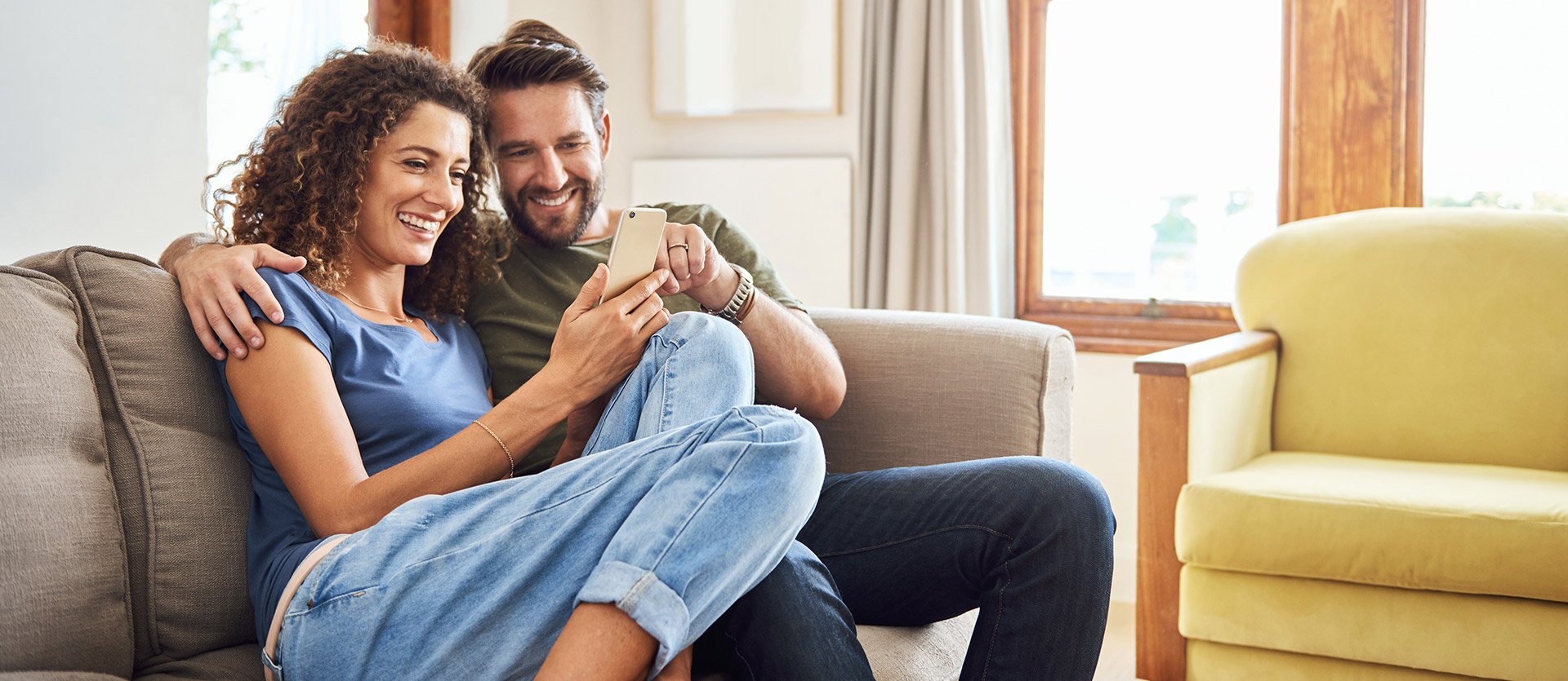 Two people sitting on the couch looking at their SELCO banking app. 