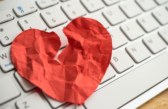 Broken paper heart sitting on a keyboard.