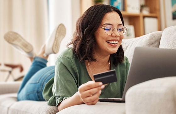 Woman sitting on her bed happy while holding her credit card.