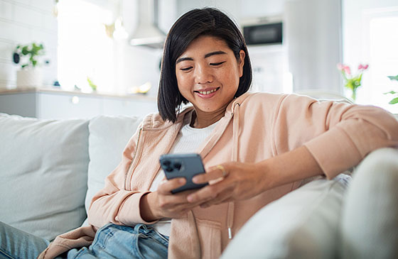 Woman sitting on a couch smiling while looking at her phone. 