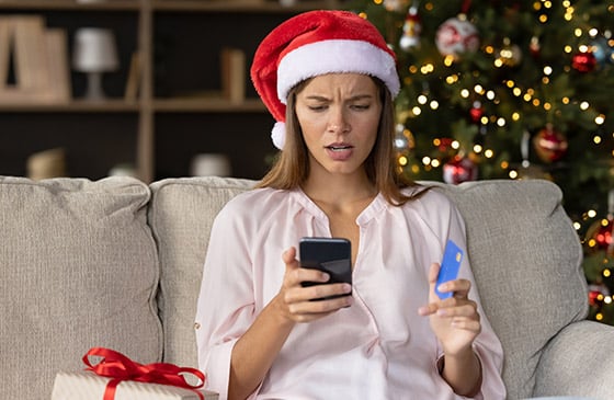 Woman looking at her phone and card worried about potentially getting scammed this holiday. 